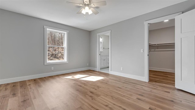 unfurnished bedroom featuring light wood finished floors, a closet, a spacious closet, ensuite bath, and baseboards