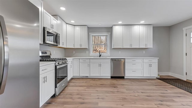 kitchen featuring stainless steel appliances, light wood-style floors, white cabinetry, a sink, and recessed lighting