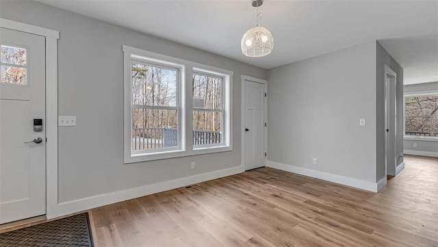 foyer entrance with light wood-type flooring, an inviting chandelier, visible vents, and baseboards