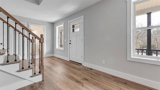 foyer entrance with visible vents, stairway, baseboards, and wood finished floors