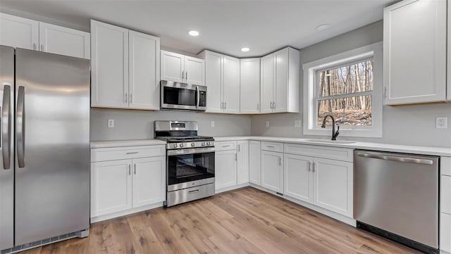 kitchen featuring appliances with stainless steel finishes, white cabinets, light countertops, and a sink