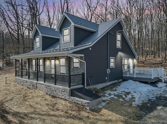 back of property at dusk featuring stone siding, metal roof, and covered porch