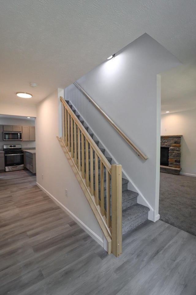 8305 Utopia Ln, East Stroudsburg, PA 18302 - stairway with baseboards, a stone fireplace, wood finished floors, and a textured ceiling