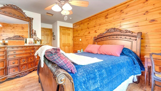 bedroom with light wood finished floors, wood walls, and a ceiling fan