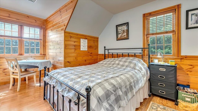 bedroom with wood walls, multiple windows, light wood-style floors, and vaulted ceiling