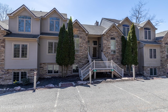 view of front of property with stone siding, stairs, a chimney, and roof with shingles