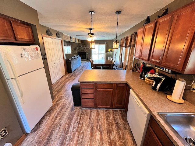 kitchen with a ceiling fan, dark wood-style flooring, a fireplace, a peninsula, and white appliances