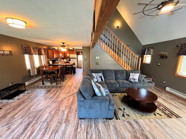 living room featuring stairway, ceiling fan, a baseboard heating unit, and light wood-style flooring