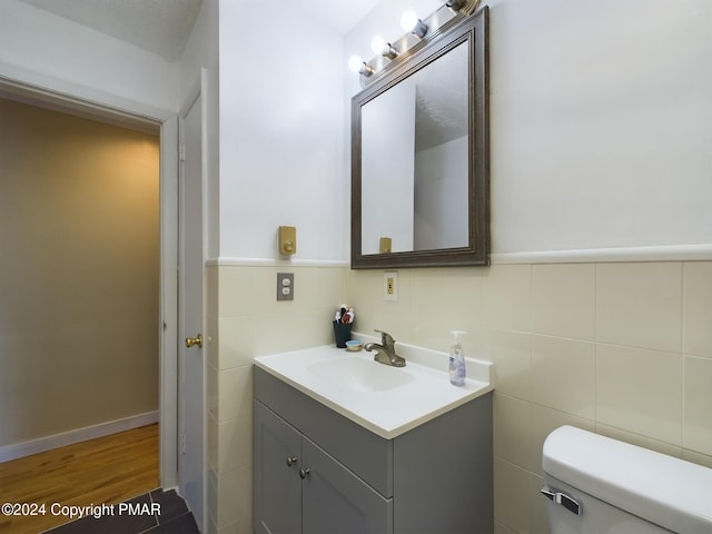 bathroom featuring toilet, a wainscoted wall, wood finished floors, vanity, and tile walls