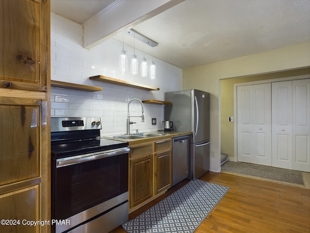 kitchen with open shelves, tasteful backsplash, appliances with stainless steel finishes, a sink, and wood finished floors