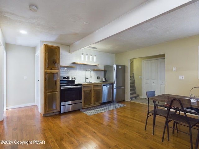 kitchen with appliances with stainless steel finishes, decorative backsplash, wood finished floors, and beamed ceiling