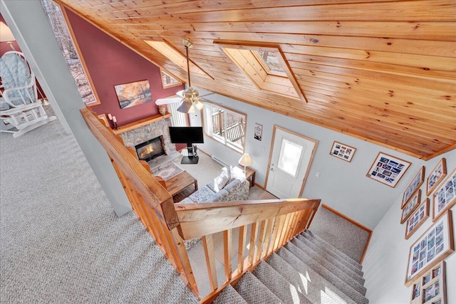 stairway featuring lofted ceiling with skylight, wood ceiling, carpet flooring, a stone fireplace, and baseboards