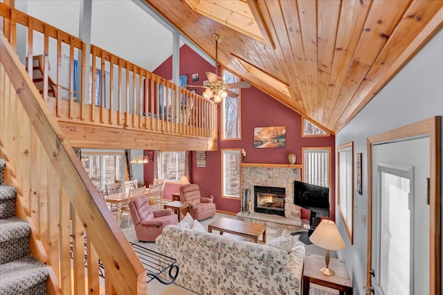 living area with a ceiling fan, wooden ceiling, stairway, a stone fireplace, and high vaulted ceiling