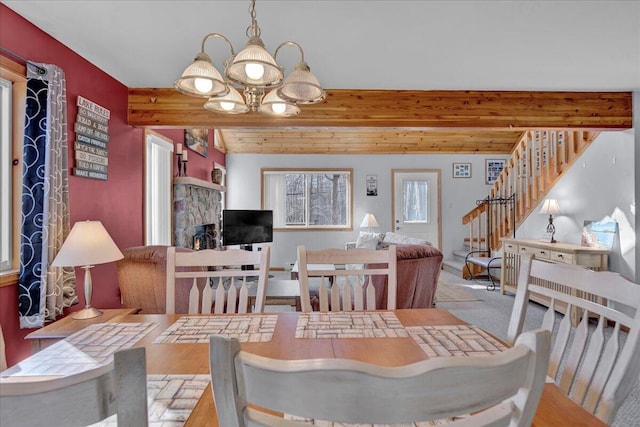 carpeted dining room featuring a notable chandelier, stairway, beam ceiling, and a stone fireplace