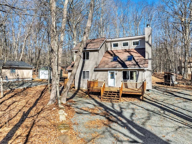 view of front facade with roof with shingles, a chimney, a deck, driveway, and an outdoor structure