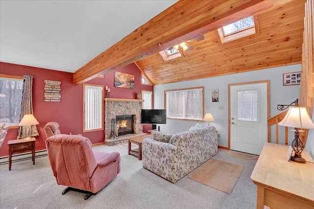 carpeted living area with a baseboard heating unit, vaulted ceiling with skylight, a stone fireplace, and baseboards