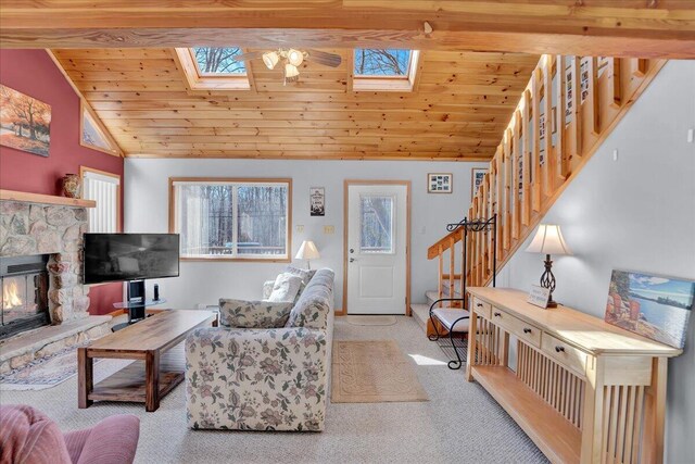 carpeted living room featuring lofted ceiling with skylight, wood ceiling, stairs, and a fireplace