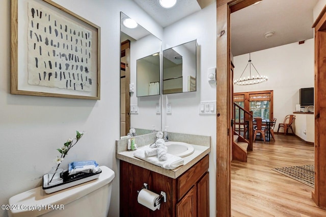 bathroom with a notable chandelier, vanity, toilet, and wood finished floors