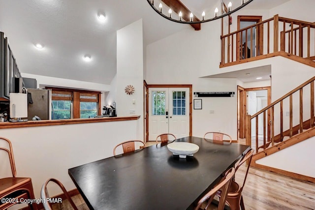 dining space with plenty of natural light, wood finished floors, stairs, french doors, and high vaulted ceiling