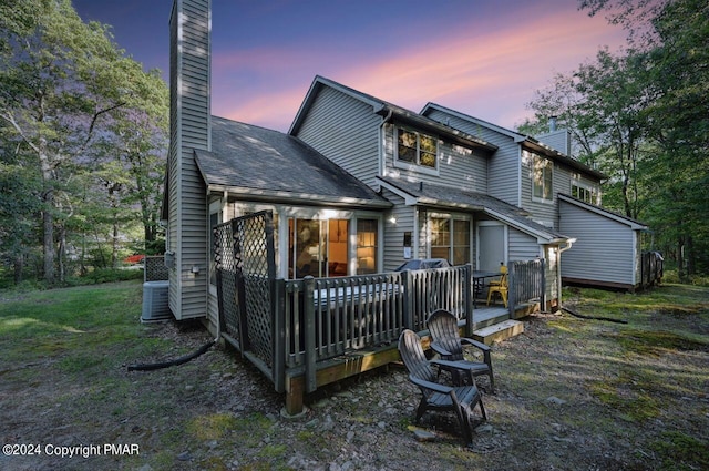 back of house at dusk with a deck, a yard, a chimney, and cooling unit