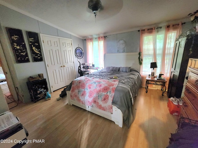 bedroom with lofted ceiling, ceiling fan, light wood-style flooring, ornamental molding, and a closet