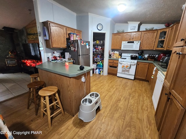 kitchen featuring a peninsula, white appliances, a breakfast bar, brown cabinets, and crown molding