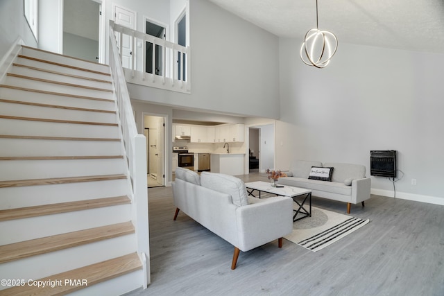 living room featuring sink, a high ceiling, heating unit, a chandelier, and light wood-type flooring