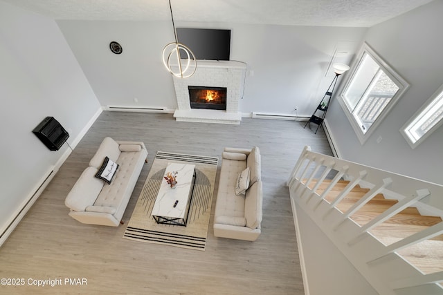 living room featuring a brick fireplace, hardwood / wood-style floors, a textured ceiling, and a baseboard heating unit