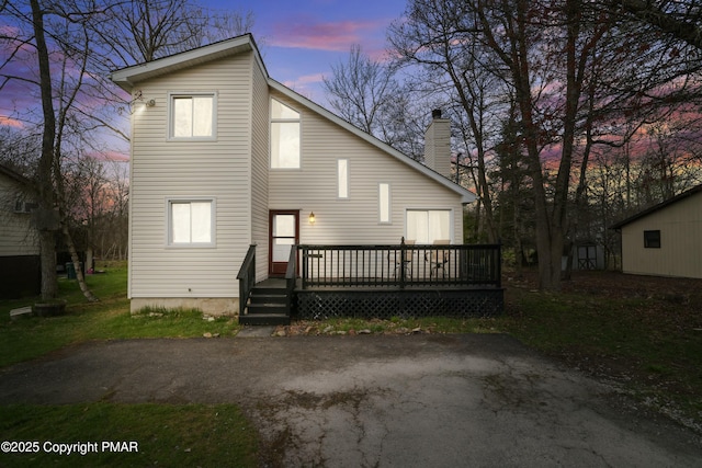 back of house at dusk featuring a deck and a chimney