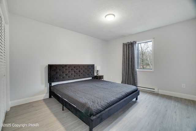 bedroom with baseboard heating, a textured ceiling, and light wood-type flooring