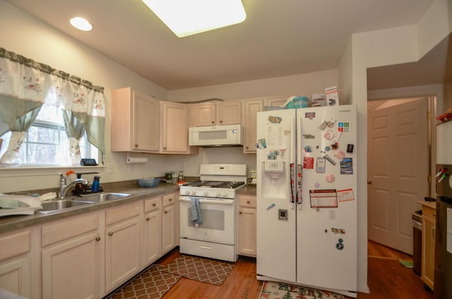 kitchen with white appliances, dark countertops, wood finished floors, and a sink