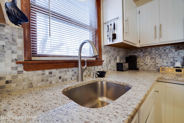 kitchen with light stone counters, backsplash, a sink, and white cabinets