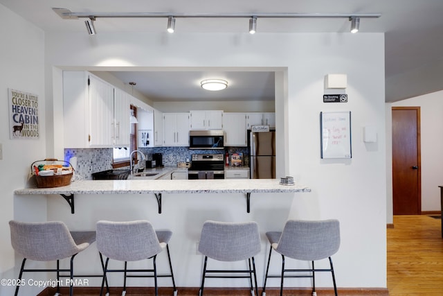 kitchen featuring stainless steel appliances, backsplash, light wood-style flooring, white cabinetry, and a peninsula