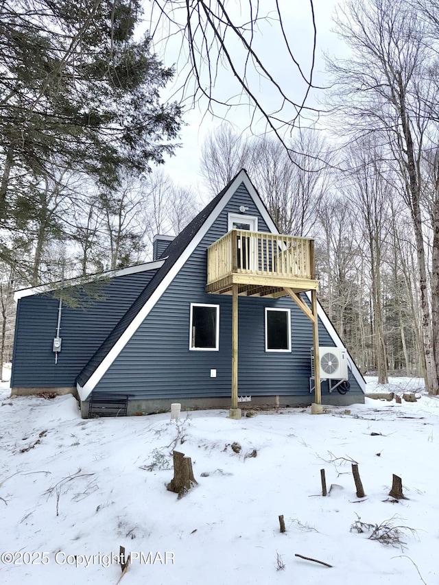 snow covered back of property with a deck, ac unit, and a garage