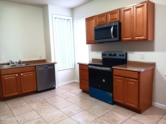 kitchen featuring stainless steel appliances, dark countertops, brown cabinets, and a sink