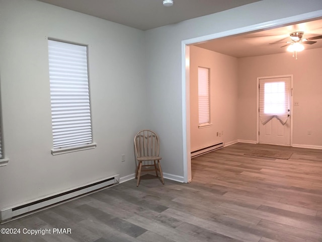 unfurnished room with baseboard heating, wood finished floors, and baseboards