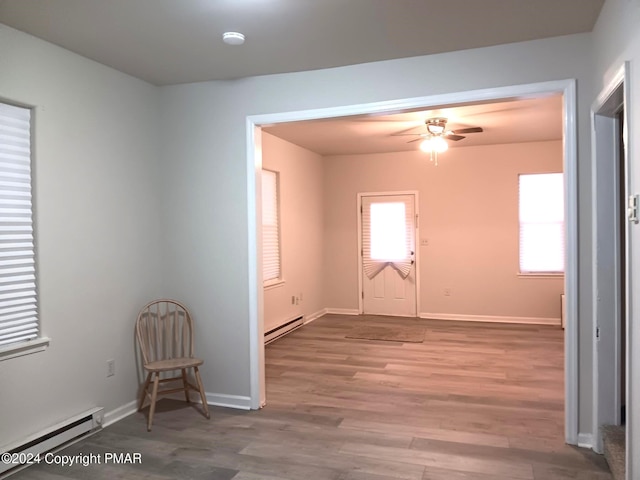 empty room with baseboard heating, wood finished floors, a ceiling fan, and baseboards