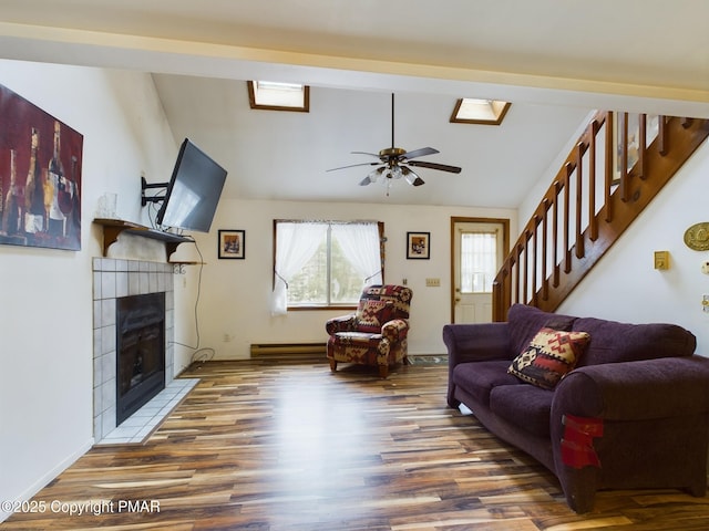 living area featuring a tile fireplace, wood finished floors, a ceiling fan, stairs, and lofted ceiling with skylight