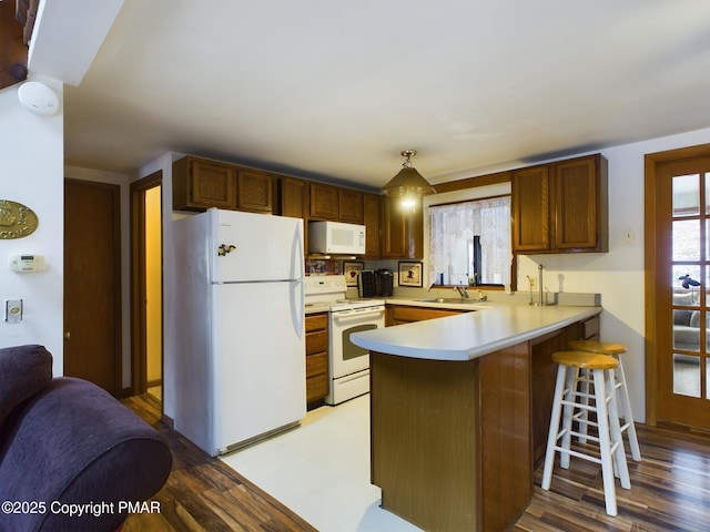 kitchen with a peninsula, white appliances, a sink, a kitchen breakfast bar, and light countertops