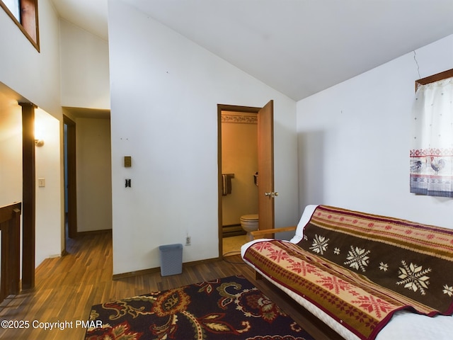 bedroom with high vaulted ceiling, a baseboard radiator, ensuite bathroom, and wood finished floors