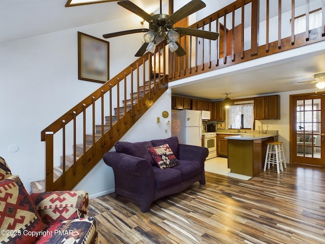 living area with a high ceiling, a ceiling fan, baseboards, light wood-style floors, and stairway