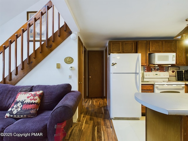 kitchen with light countertops, brown cabinetry, open floor plan, wood finished floors, and white appliances