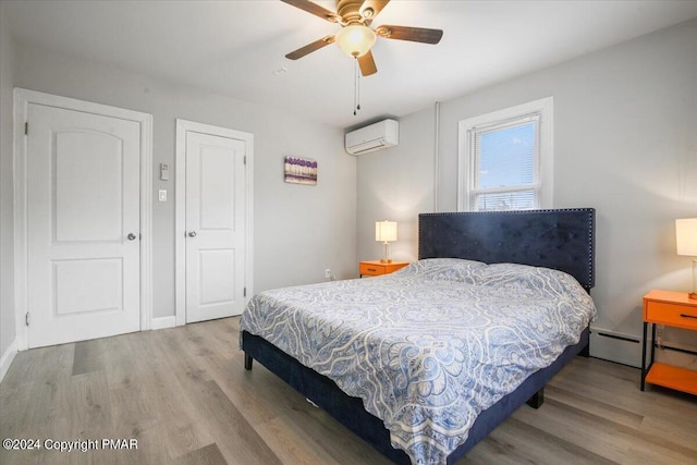 bedroom featuring a baseboard heating unit, a ceiling fan, a wall unit AC, and wood finished floors