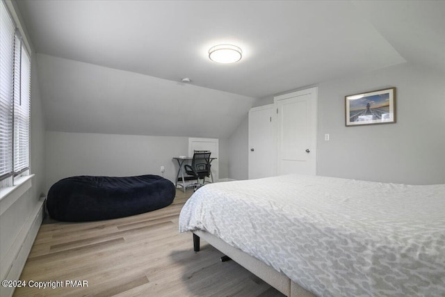 bedroom with lofted ceiling, baseboard heating, and wood finished floors