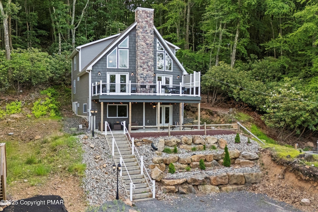 view of front of house featuring a deck, french doors, stairway, a chimney, and a wooded view