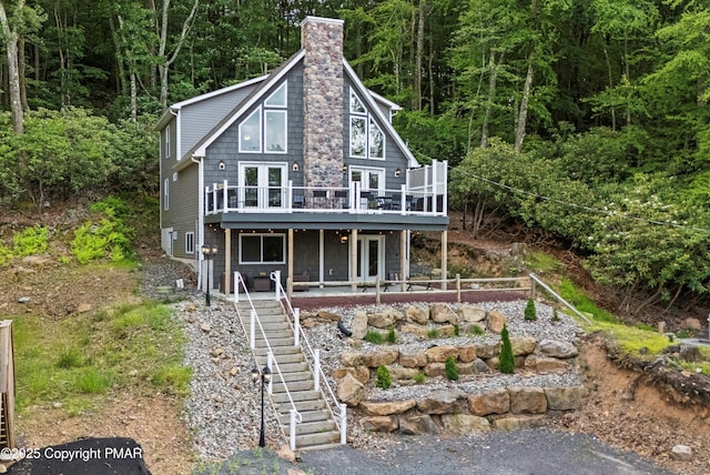 view of front of house featuring a deck, french doors, stairway, a chimney, and a wooded view