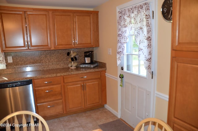 kitchen with brown cabinetry, dark stone countertops, tasteful backsplash, and stainless steel dishwasher