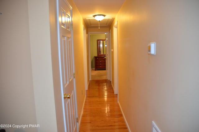 hall featuring baseboards, attic access, and light wood-style floors