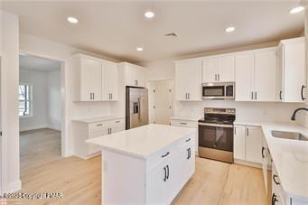 kitchen featuring stainless steel appliances, a sink, light countertops, a center island, and light wood finished floors