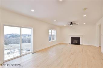 unfurnished living room featuring recessed lighting, a fireplace with raised hearth, light wood-style floors, a ceiling fan, and baseboards